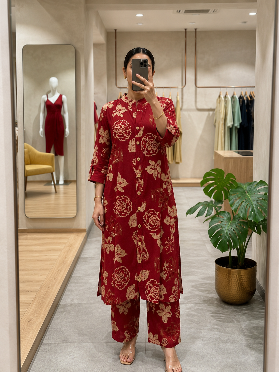 Person wearing a red floral dress taking a mirror selfie in a store.